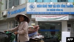 Một người bán hàng rong đi ngang qua một chi nhánh Saigon Commercial Bank, Hà Nội, 6 tháng 12, 2011. Hình minh hoạ.